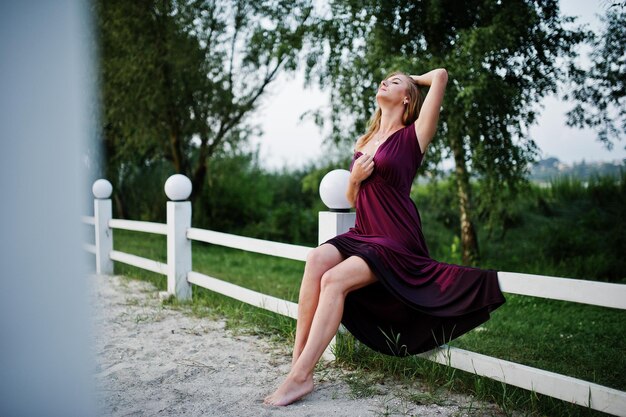 Blonde sensual woman in red marsala dress posing on beach of resort