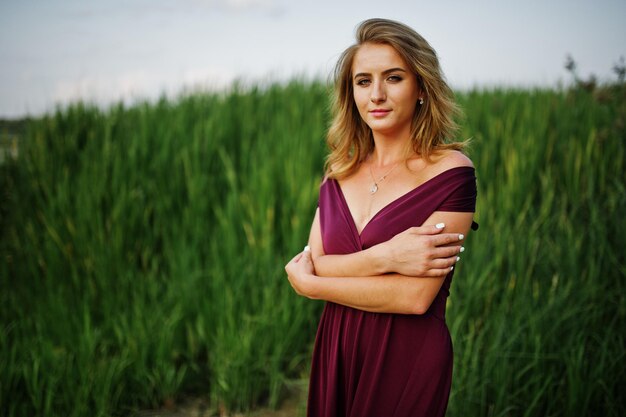 Blonde sensual woman in red marsala dress posing in the reeds