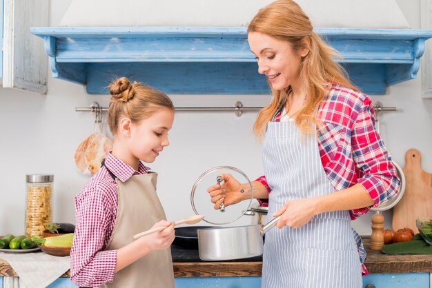 金髪の笑みを浮かべて女性が台所で彼女の娘に鍋を見せて