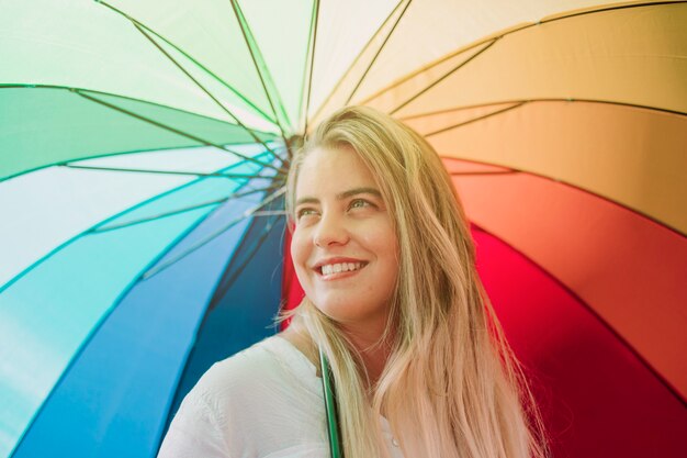 虹の傘を保持している金髪の笑顔若い女性