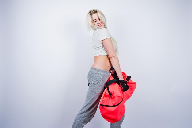 Блондинка спортивная девушка с большой спортивной сумкой позирует в студии на белом фоне