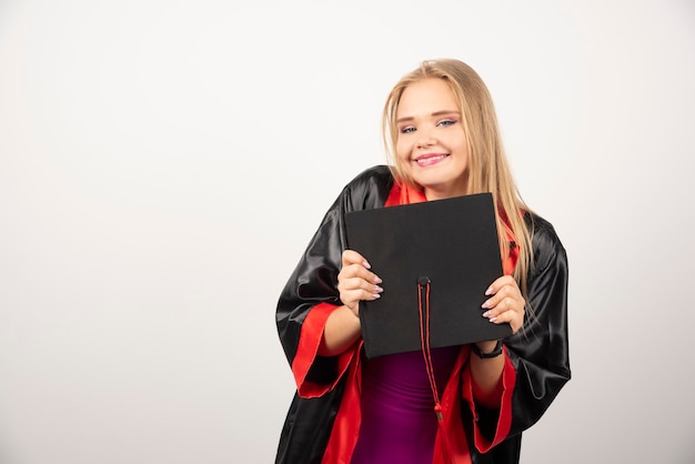 Blonde student posing with her cap on white.