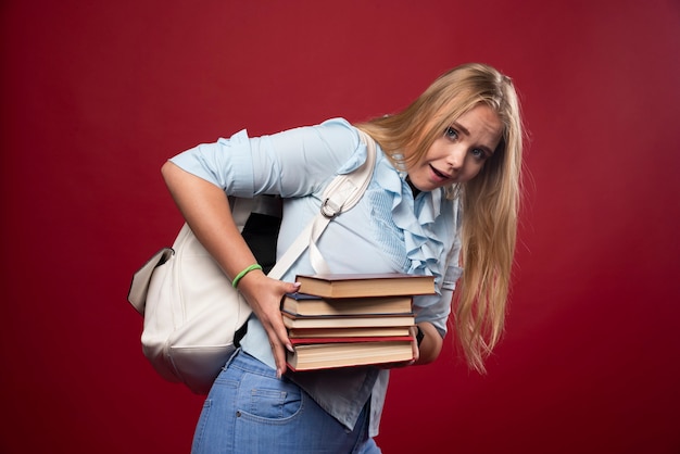 本の重い山を保持し、疲れているように見える金髪の学生女性。