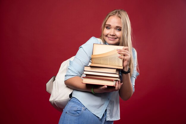 Блондинка студент женщина, держащая кучу книг и выглядит позитивно.