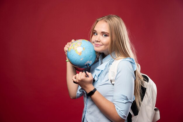 Blonde student woman holds a globe and looks positive.