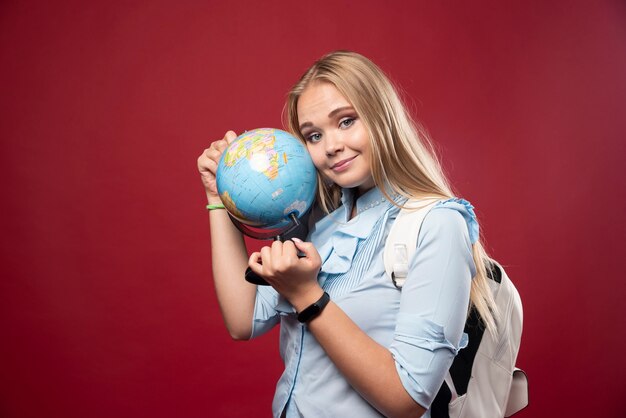Blonde student woman holds a globe and looks positive.