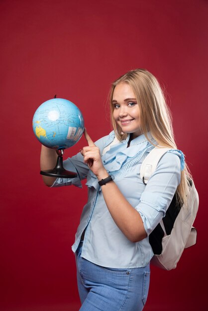 Белокурая женщина студента держит глобус и указывая место.