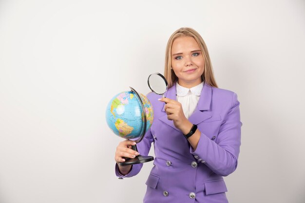 Blonde teacher looking at globe with magnifying glass. High quality photo