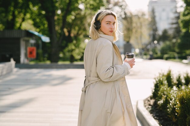 La bionda cammina nella città dell'estate con la tazza di caffè