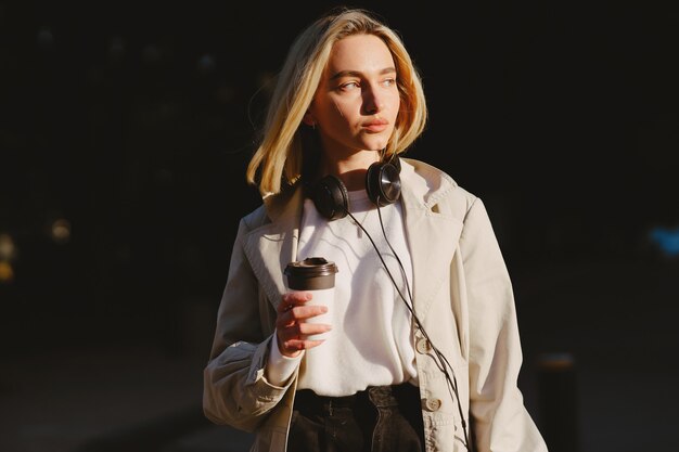 Blonde walks in summer city with cup of coffee