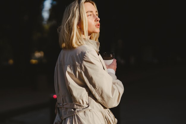 Blonde walks in summer city with cup of coffee