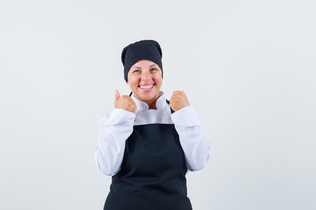 Blonde woman in black cook uniform clenching fists and looking pretty