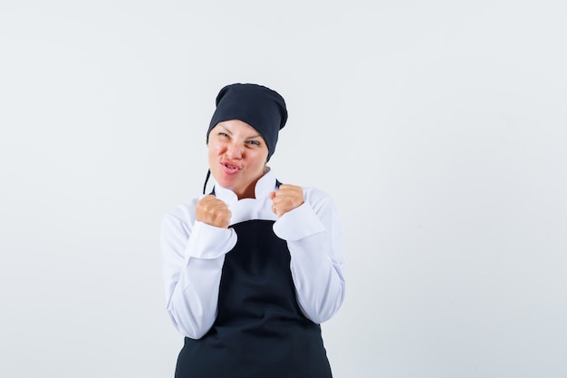 Blonde woman in black cook uniform showing winner pose and looking pretty