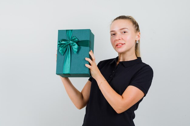 Blonde woman in black t-shirt holding gift box and smiling and looking happy