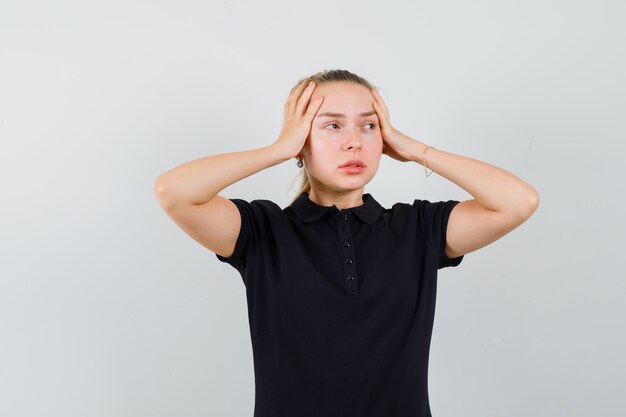 Blonde woman in black t-shirt holding her hands on her head and looking annoyed