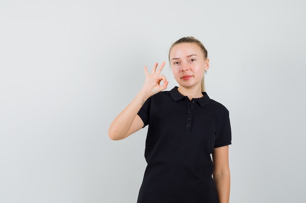 Blonde woman in black t-shirt showing ok sign and looking happy