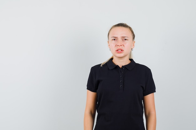 Blonde woman in black t-shirt trying to say something and looking confused