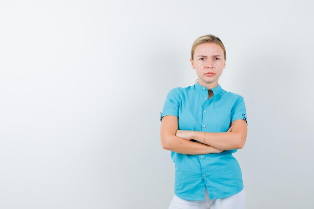 Blonde woman in blue blouse keeping arms folded and looking serious isolated