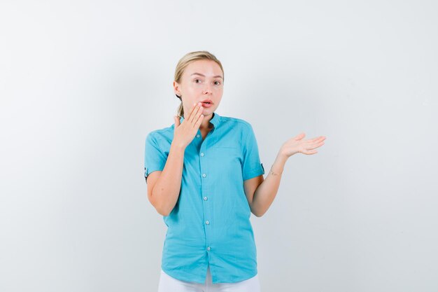 Blonde woman in blue blouse keeping hand near mouth isolated