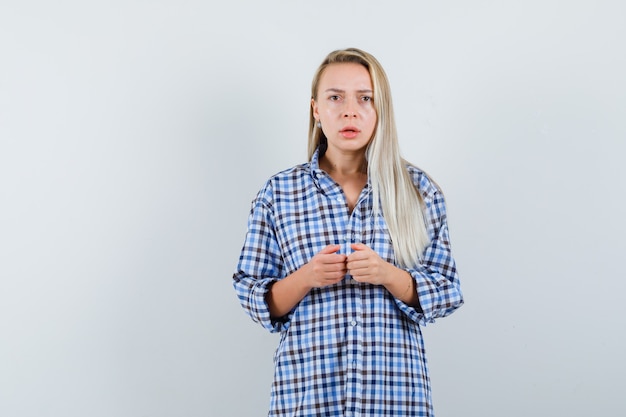 Donna bionda in camicia a quadretti blu a quadretti tenendosi per mano mentre gioca alla console e sembra tormentata, vista frontale.