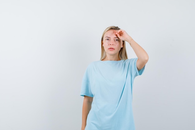 Blonde woman in blue t-shirt holding hand over head and looking serious