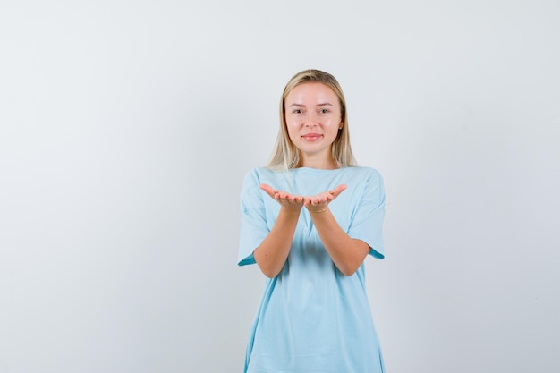 想像上の何かを持っているように手を伸ばす青いTシャツのブロンドの女性