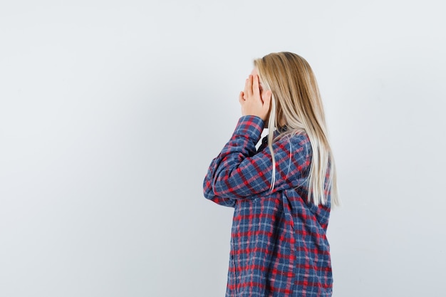 Blonde woman in checked shirt covering face with hands and looking tired , front view.