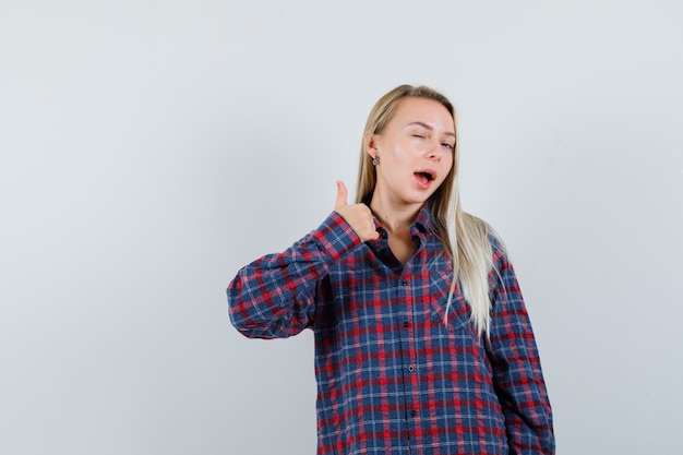 Free photo blonde woman in checked shirt showing thumb up and winking and looking attractive , front view.