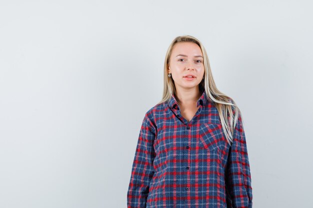 Blonde woman in checked shirt standing straight and posing at camera and looking optimistic , front view.