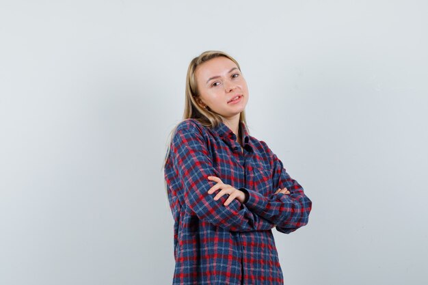 Blonde woman in checked shirt standing with arms crossed and looking happy , front view.