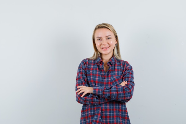 Blonde woman in checked shirt standing with arms crossed and looking happy , front view.