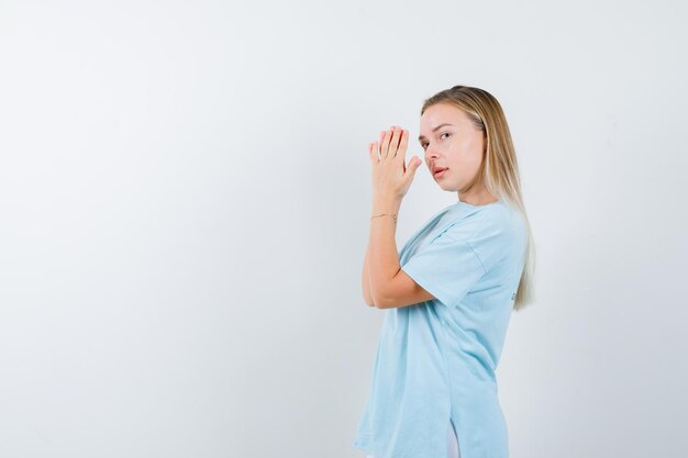 Free photo blonde woman clasping hands in font of face, looking over shoulder