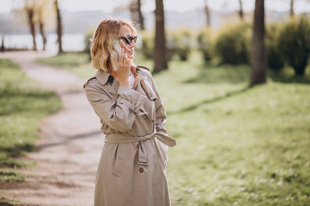Blonde woman in coat outside in park using phone