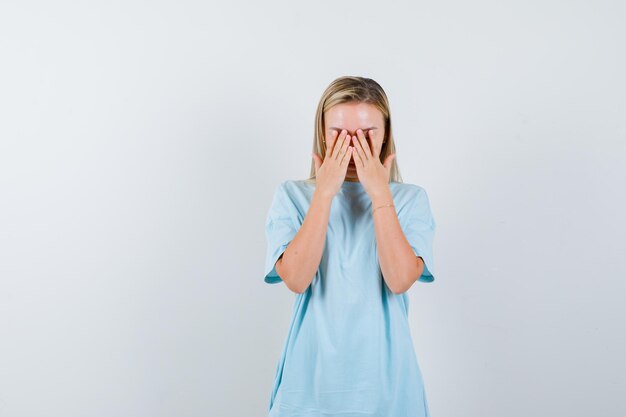 Blonde woman covering face with hands in blue t-shirt and looking ashamed