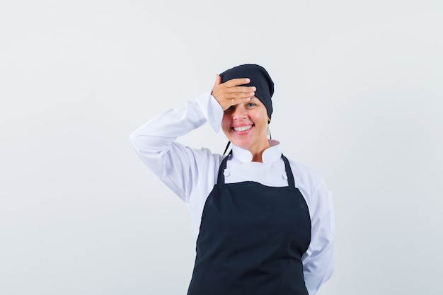 Blonde woman covering forehead with hand in black cook uniform and looking pretty