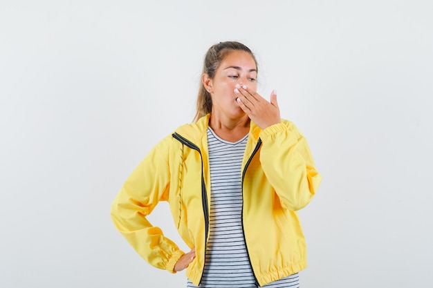 Free photo blonde woman covering mouth with hands in yellow bomber jacket and striped shirt and looking surprised
