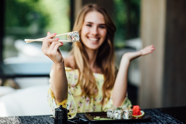 Blonde woman eating sushi using chopsticks