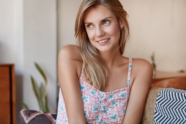 Blonde woman in floral dress sitting on couch