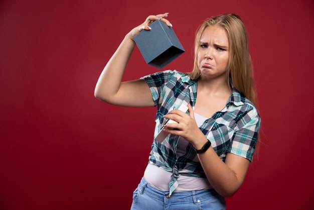 Blonde woman gets sad and confused while opening a gift box.