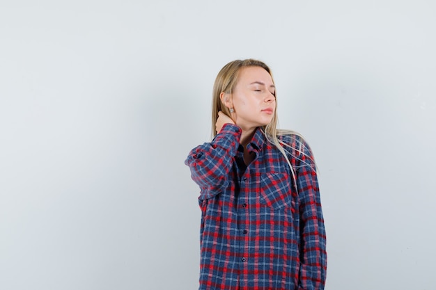 Blonde woman having neckache in checked shirt and looking exhausted. front view.