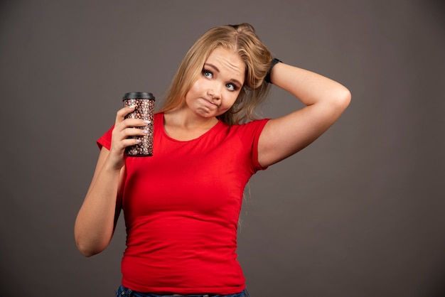 Blonde woman holding at cup of coffee on black wall.