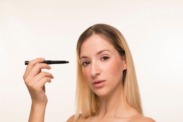 Blonde woman holding eyeliner near face