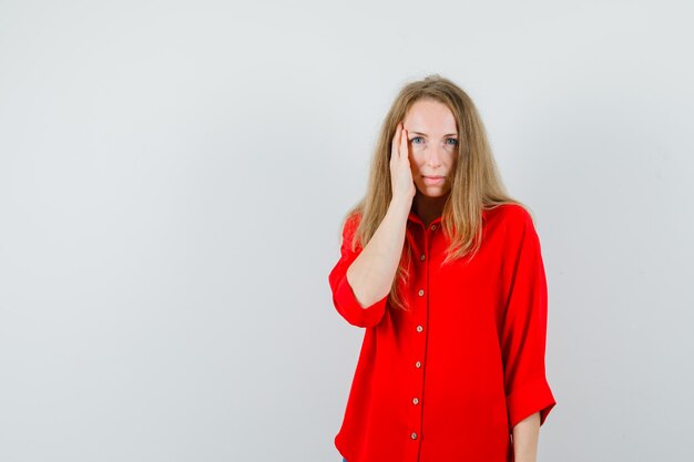 Blonde woman holding hand on cheek in red shirt and looking calm ,