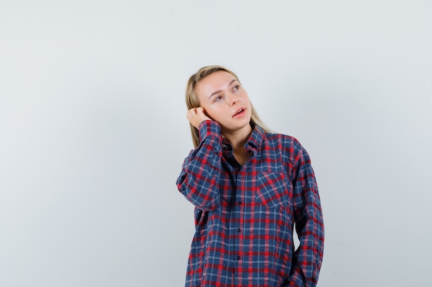 Donna bionda che tiene la mano sull'orecchio, fingendo di parlare al telefono in camicia a quadri e guardando concentrato. vista frontale.