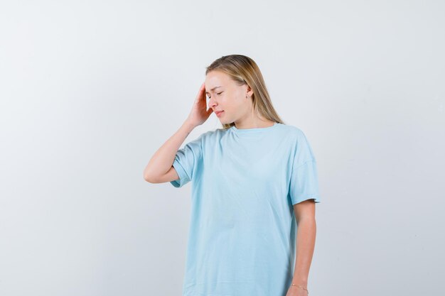 Blonde woman holding hand on temple in blue t-shirt and looking cute