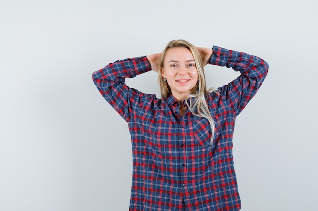 Blonde woman holding hands on head, posing at camera in checked shirt and looking attractive , front view.