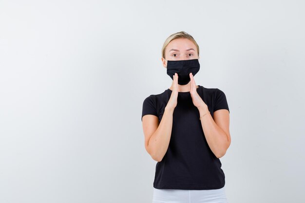 Blonde woman holding hands near mouth to tell secret in black t-shirt, white pants