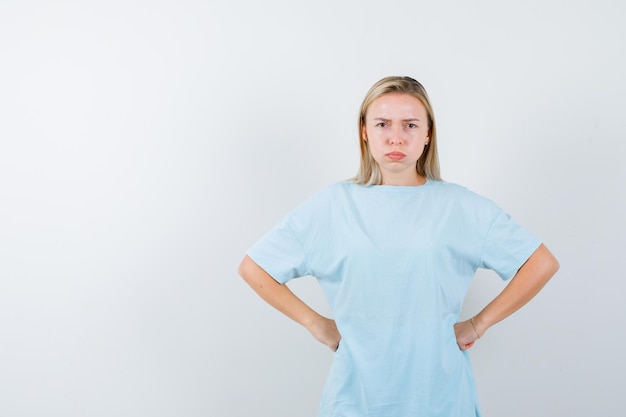 Free photo blonde woman holding hands on waist, puffing cheeks in blue t-shirt