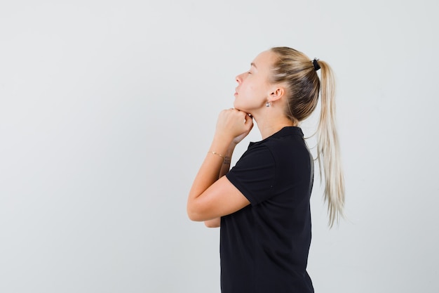 Blonde woman holding her hands under chin in black t-shirt and looking relaxed