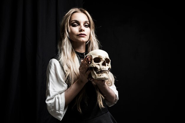 Blonde woman holding skull on black background